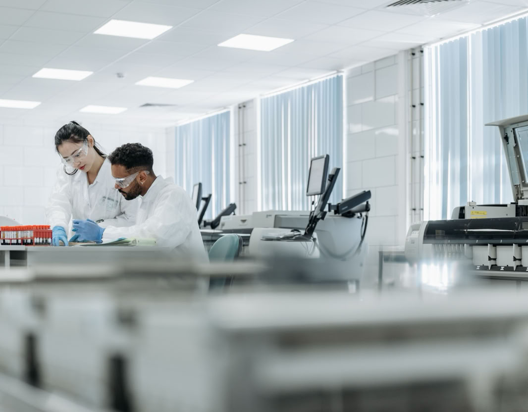Two scientists working in a high-tech laboratory setting, wearing protective eyewear and gloves.